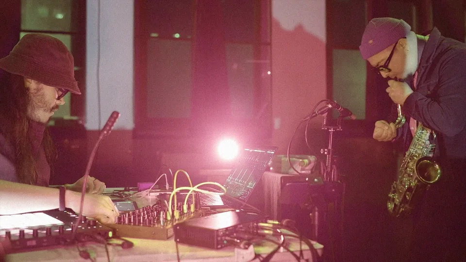 Jorge Care at the electronics and César Vidal on saxophone under pink light, performing alea II.