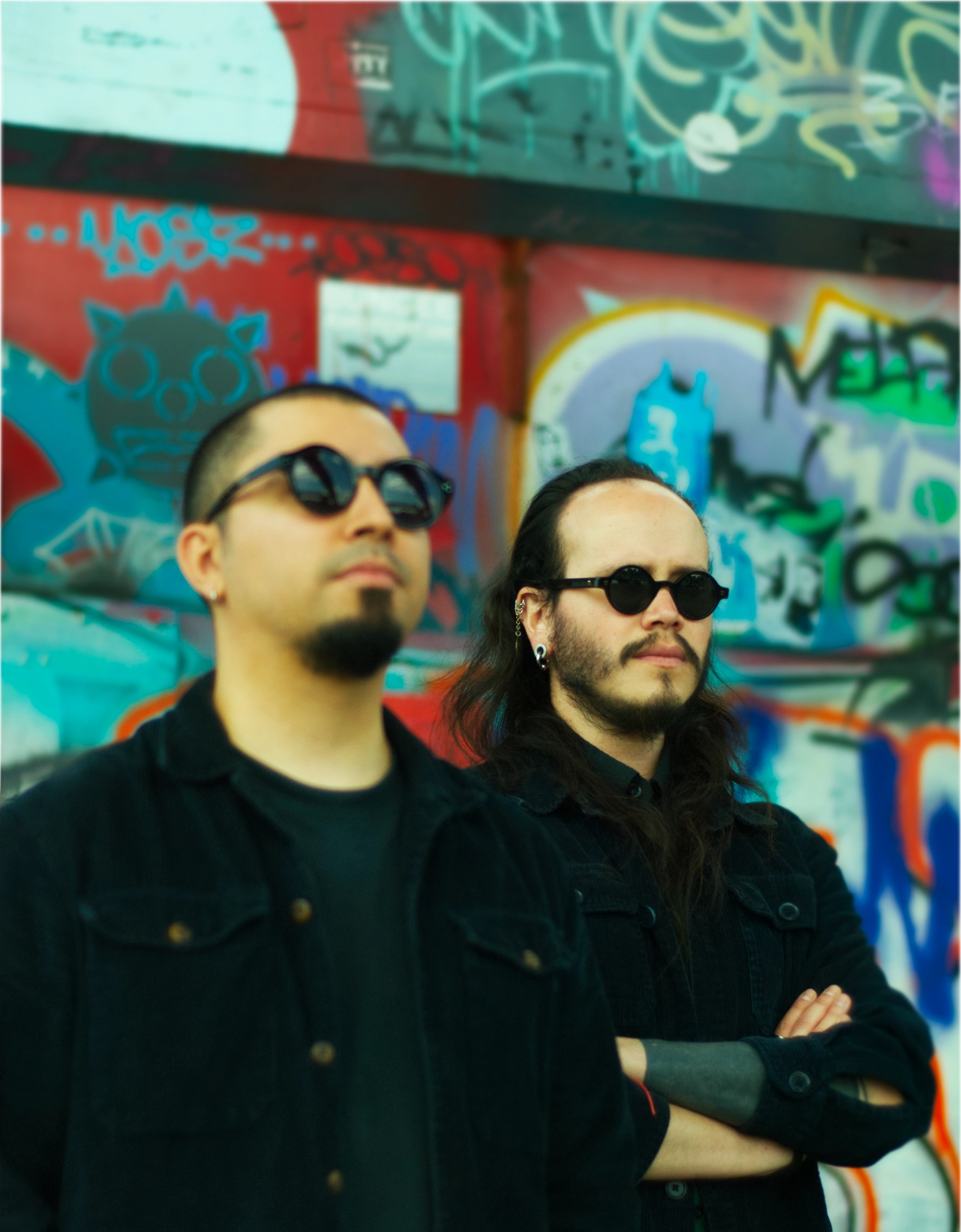 Jorge Care and César Vidal in front of a wall of graffiti.